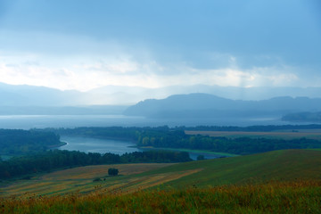 Fototapeta premium landscape with storm clouds, green and yellow meadow a lake 