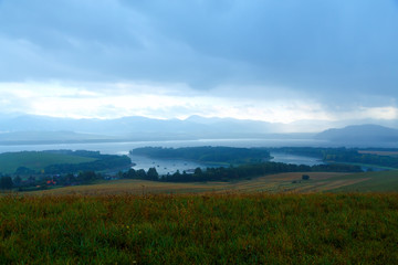 Obraz premium landscape with storm clouds, green and yellow meadow a lake 