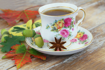 Cup of tea in vintage cup, star anise, autumn leaves and acorns on rustic wooden surface

