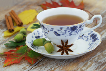 Cup of tea in vintage cup, star anise, autumn leaves and acorns on rustic wooden surface
