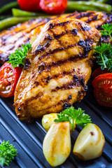 Grilled chicken breast in different variations with cherry tomatoes, green French beans, garlic, herbs, cut lemon on a wooden board or teflon pan. Traditional cuisine. Grill kitchen. 