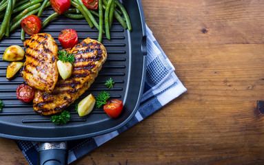 Grilled chicken breast in different variations with cherry tomatoes, green French beans, garlic, herbs, cut lemon on a wooden board or teflon pan. Traditional cuisine. Grill kitchen. 