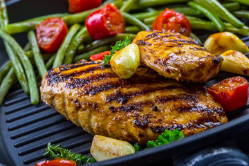 Grilled chicken breast in different variations with cherry tomatoes, green French beans, garlic, herbs, cut lemon on a wooden board or teflon pan. Traditional cuisine. Grill kitchen. 