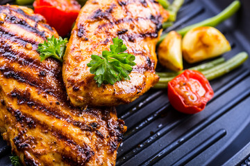 Grilled chicken breast in different variations with cherry tomatoes, green French beans, garlic, herbs, cut lemon on a wooden board or teflon pan. Traditional cuisine. Grill kitchen. 