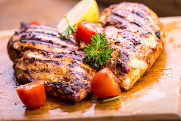 Grilled chicken breast in different variations with cherry tomatoes, green French beans, garlic, herbs, cut lemon on a wooden board or teflon pan. Traditional cuisine. Grill kitchen. 