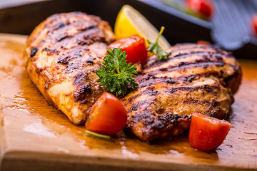 Grilled chicken breast in different variations with cherry tomatoes, green French beans, garlic, herbs, cut lemon on a wooden board or teflon pan. Traditional cuisine. Grill kitchen.  - obrazy, fototapety, plakaty