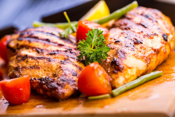 Grilled chicken breast in different variations with cherry tomatoes, green French beans, garlic, herbs, cut lemon on a wooden board or teflon pan. Traditional cuisine. Grill kitchen. 