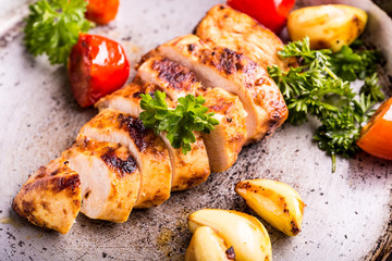 Grilled chicken breast in different variations with cherry tomatoes, green French beans, garlic, herbs, cut lemon on a wooden board or teflon pan. Traditional cuisine. Grill kitchen. 