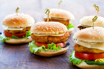 Appetizing mini chicken burgers on wooden surface.