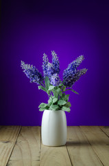 Lavender flowers in white vase on a purple background.