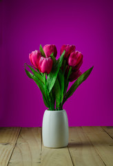 Red tulips in a vase pink background