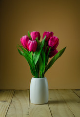Red tulips in a vase brown background