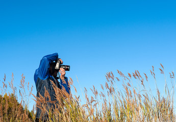 photographer among the tall grass on the background of blue sky