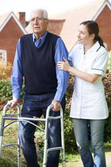 Carer Helping Senior Man To Walk In Garden Using Walking Frame