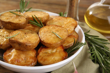 Delicious baked potato with rosemary in bowl on table close up