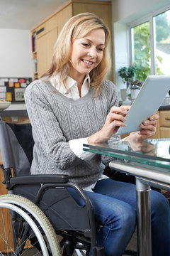 Disabled Woman In Wheelchair Using Digital Tablet At Home