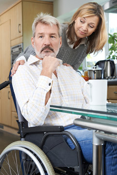 Woman Comforting Depressed Man In Wheelchair At Home