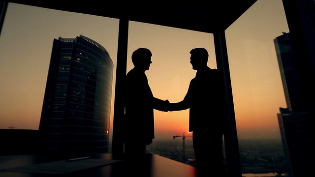 silhouette of two businessmen talking and shaking hands standing