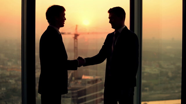 silhouette of two businessmen talking and shaking hands standing