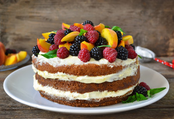 Naked cake with cream, decorated with raspberries, blackberries, peaches