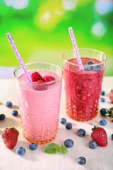 Glasses of berry smoothie on wooden table on blurred background