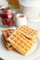 Sweet homemade waffles with fresh strawberries on plate, on light background
