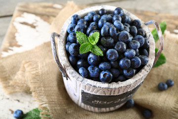 Tasty ripe blueberries with green leaves in bucket on table close up