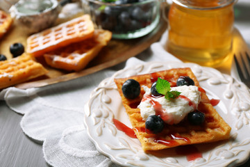 Sweet homemade waffles on plate, on color wooden background