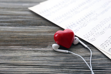 Earphones with red heart and music notes on wooden background