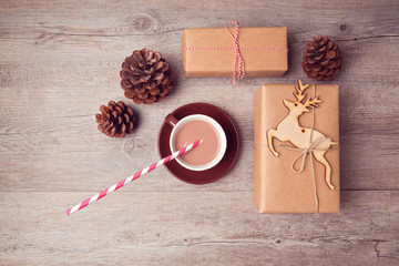 Christmas handmade gift boxes with cup of chocolate and pine corn on wooden table. View from above