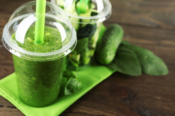 Green vegetable and fruit salad and healthy fresh drink in plastic cups on wooden background. Colorful diet concept