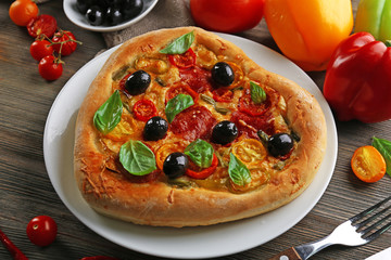 Heart shaped pizza served on plate on wooden background