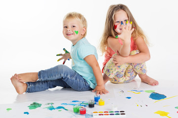 Two childs are drawing by aquarelle paints on white paper