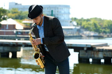Young man playing on saxophone on the riverside