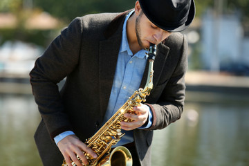 Naklejka premium Young man playing on saxophone on the riverside