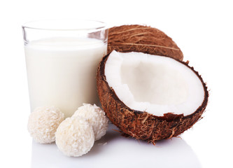 Candies in coconut flakes, glass of milk and fresh coconut isolated on white