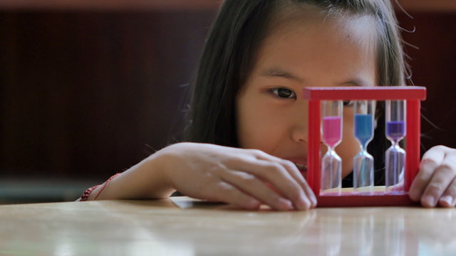 Little Asian child looking at hourglass in class
