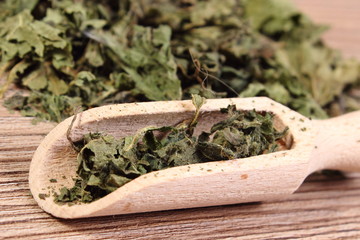 Dried nettle with spoon on wooden surface