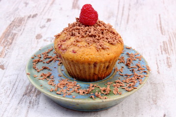 Baked muffins with raspberries and grated chocolate on wooden background, delicious dessert