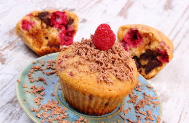 Baked muffins with raspberries and grated chocolate on wooden background, delicious dessert