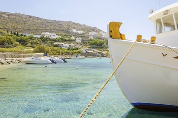 Fishing boats docked at Ornos beach in Greece. A view of the crystal clear blue sea at the greek island Mykonos, and whitewashed houses on the hill slope. A typical, idyllic summer holiday beach scene © f8grapher