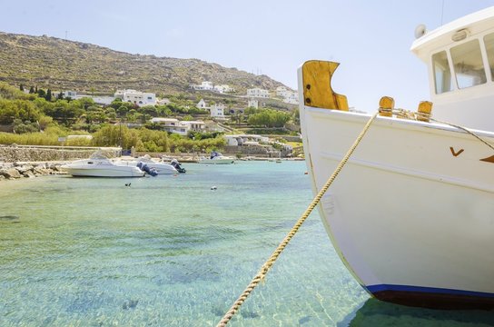 Fishing boats docked at Ornos beach in Greece. A view of the crystal clear blue sea at the greek island Mykonos, and whitewashed houses on the hill slope. A typical, idyllic summer holiday beach scene