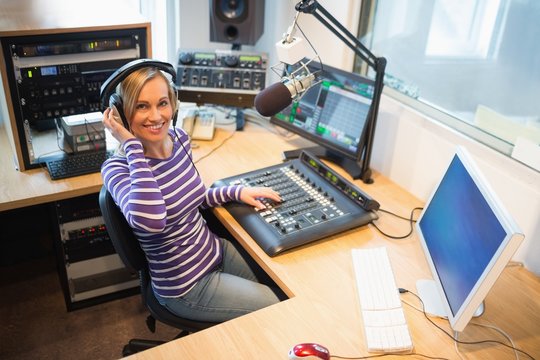 Happy female radio host at sound mixer desk in studio