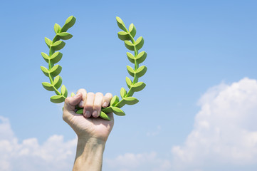 Hand of athlete holding laurel wreath in bright sunny blue sky