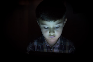 Niño iluminado por la luz de la pantalla de su tablet o e-book