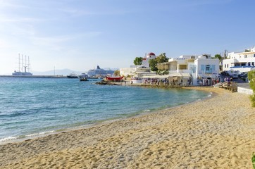 The coastline of Chora in Mykonos, Greece. Typical greek island whitewashed houses on the shore and seaview golden sand promenade overlooking the Aegean sea and calm clean blue water. © f8grapher