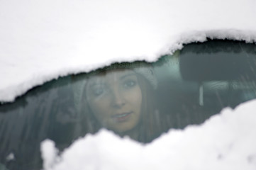 Junge Frau schaut durch die teilweise verschneite Windschutzscheibe ihres Autos