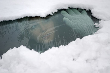 Junge Frau schaut durch die teilweise verschneite Windschutzscheibe ihres Autos