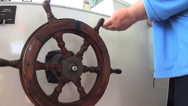 Boat wheel being steered and turned by a crew member.