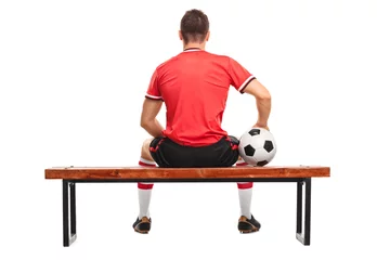 Foto op Canvas Football player holding a ball and sitting on a bench © Ljupco Smokovski